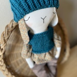 Doudou fait main Alex en coton recyclé, portant un bonnet bleu tricoté, une chemise florale vintage et un pantalon en velours marron, présenté dans un décor chaleureux et naturel.